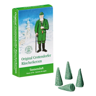 Grüne Verpackung der Original Crottendorfer Räucherkerzen mit der Aufschrift ‚Tannenduft‘. Auf der Vorderseite ist eine Illustration eines Mannes in grüner Kleidung mit Spazierstock vor einer verschneiten Dorfkulisse zu sehen. Unten auf der Schachtel stehen die Übersetzungen ‚Scent of Fir‘ und ‚Senteur de sapin‘. Neben der Verpackung liegen vier grüne, kegelförmige Räucherkerzen.