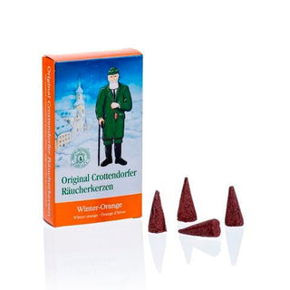 Rechteckige Verpackung der Original Crottendorfer Räucherkerzen ‚Winter-Orange‘ mit winterlicher Illustration: Ein Mann in grüner Kleidung und Mütze hält einen Stock, im Hintergrund ist eine verschneite Landschaft mit einem Gebäude zu sehen. Der untere Teil der Verpackung ist orangefarben und trägt die Aufschrift ‚Original Crottendorfer Räucherkerzen‘ sowie ‚Winter-Orange‘ in Deutsch, Englisch und Französisch. Neben der Verpackung liegen vier dunkelrote, kegelförmige Räucherkerzen.