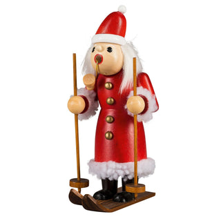 Der rot gekleidete Weihnachtsmann fährt auf seinen Skiern. In den Händen hält er die Skistöcke und im Mund hat er seine Pfeife. Sein Mantel wird verziehrt von goldfarbenen Knöpfen.