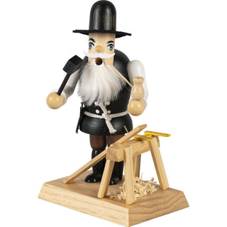 Farbiges Räuchermännchen im Motiv eines Zimmermannes. In der einen Hand hält er einen Hammer und in der anderen seine Pfeife. Maßstab, Holzbock, Brett und Spähne sind auch auf dem Sockel mit abgebildet.