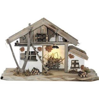 Weihnachtskrippe mit LED-Beleuchtung. Die Kriipe im Motiv des Stalles ist naturfarben. Im Stall befindet sich eine Futterraufe mit Stroh. Vor dem Stall liegen Holzstapel und eine Treppe führt in die obere Etage.