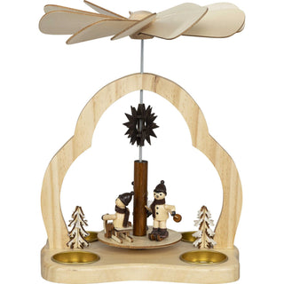 Naturfarbene Weihnachtspyramide mit 4 Pyramidenteelichtern. Auf der Pyramide befinden sich 3 Winterkinder beim Wintersport. Rechts und links wird die Pyramide mit 2 kleinen Winterbäumchen verziehrt,