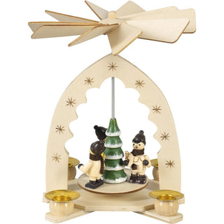 Naturfarbene Weihnachtspyramide mit Winterkinder für 4 Pyramidenkerzen. Auf dem Pyramidenteller stehen 3 kleine Winterkinder. In der Mitte befindet sich ein grünfarbener, beschneiter Tannenbaum. Der Pyramidenbogen ist mit Sternen verziert.